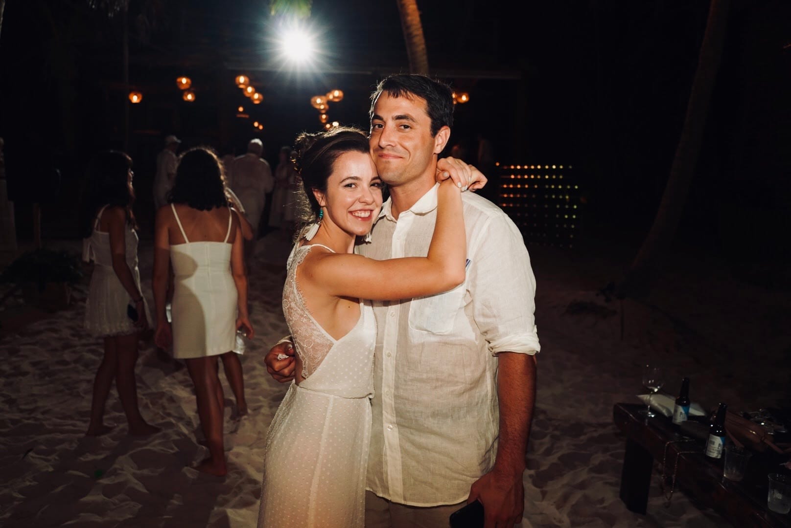 Megan and James embracing on the sand at a candlelit beach party at night